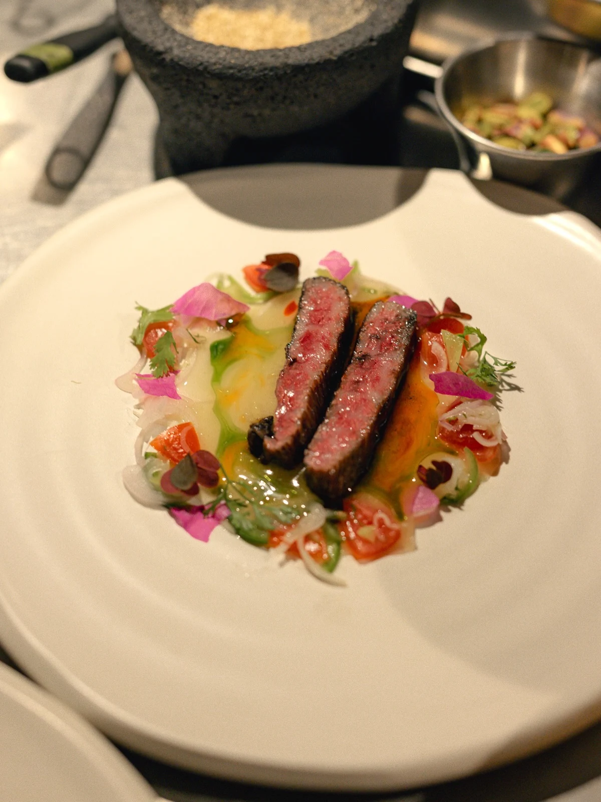 Dos piezas de Wagyu con vegetales y flores en un plato blanco.