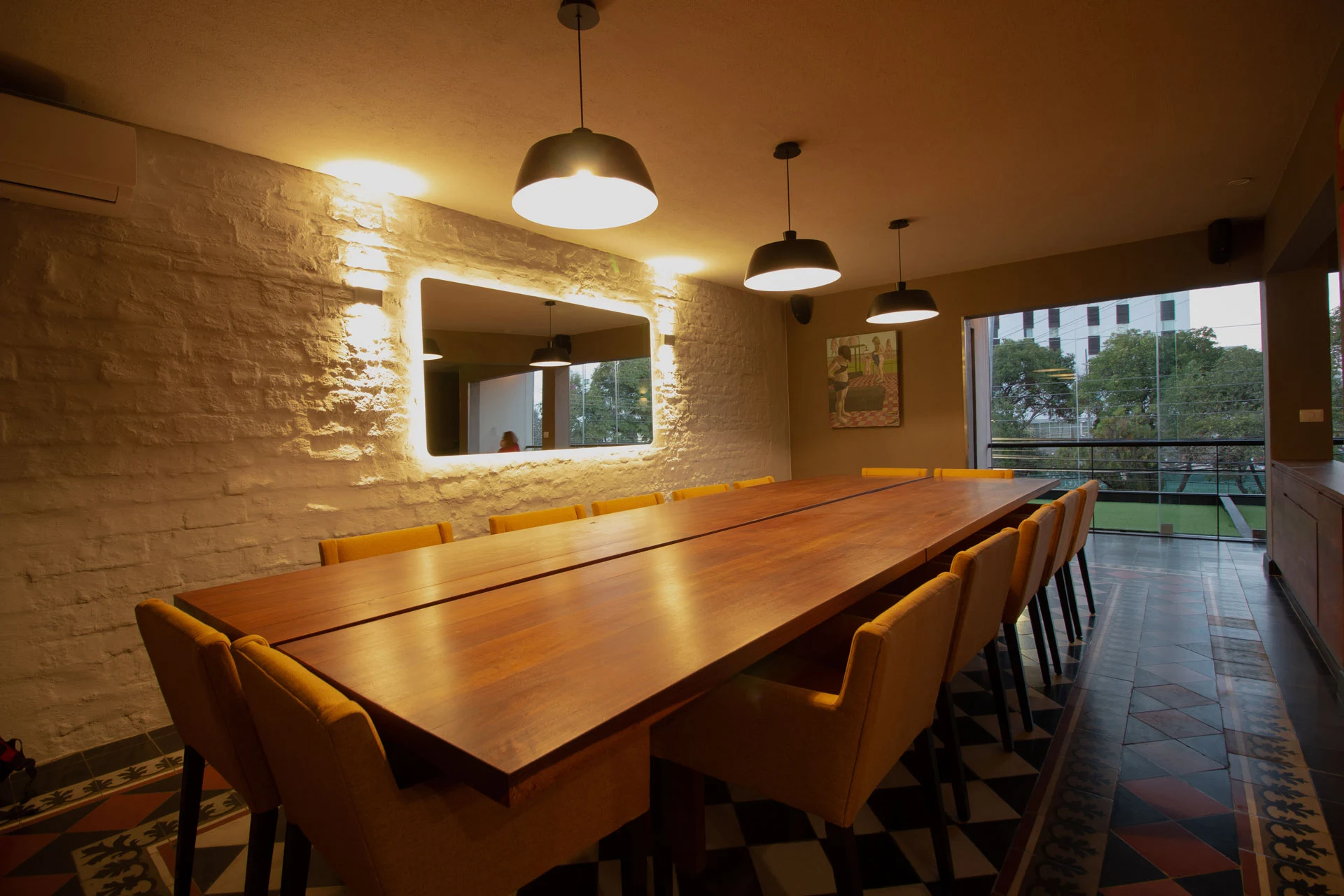 Salón privado de Alcalde con mesa de madera, sillas mostaza y lámparas colgantes.